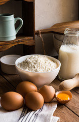 Baking ingredients flour milk eggs rolling pin on wood kitchen table, rustic interior, cozy atmosphere