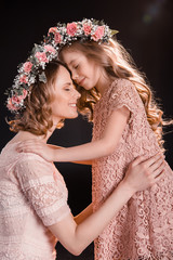 Happy mother and daughter in floral wreaths hugging and touching foreheads