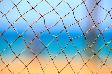 Fishing net at summer seaside on blue sky, sea and sandy beach abstract background