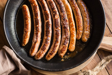 Variety of fried or roasted sausages with golden crust in iron cast pan, wood kitchen table, top view