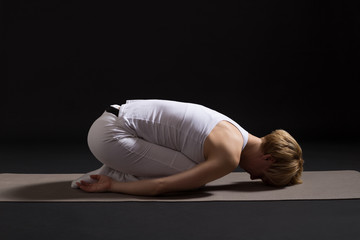 Woman exercising yoga indoor on black background,Child pose/Balasana