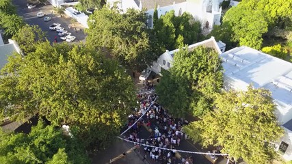 Aerial flight top down view over streets with neighborhood party people dressed up in white clothing small village party gathering after a wedding also showing trees and some buildings below 4k