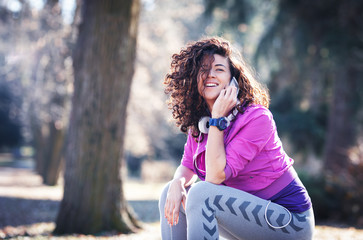 Young female sitting on bench at the park and relaxing after jogging.Talking on smart phone.