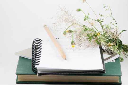 Flowers, pencil, book and a notebook on a desk.