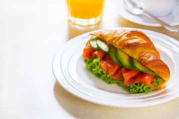 croissant sandwich with salmon and avocado, coffee and orange juice on a white background