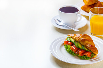 croissant sandwich with salmon and avocado, coffee and orange juice on a white background