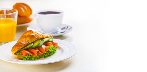 croissant sandwich with salmon and avocado, coffee and orange juice on a white background