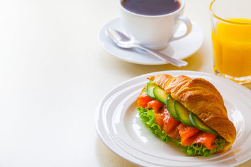 croissant sandwich with salmon and avocado, coffee and orange juice on a white background