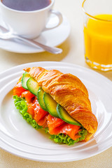 croissant sandwich with salmon and avocado, coffee and orange juice on a white background
