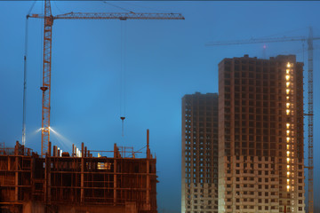 Cranes on a large construction site, unfinished multi-storey houses, foggy evening twilight