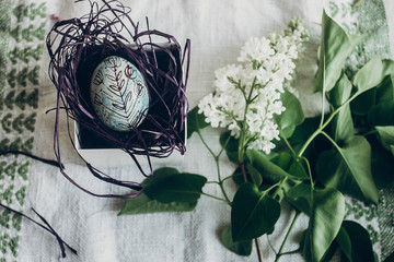 happy easter. easter egg in nest with floral and chick ornaments on rustic background with lilac flowers. top view. space for text.  greeting card concept. stylish decoration