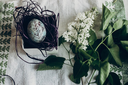 easter egg in nest with floral and chick ornaments on rustic background with lilac flowers. top view. space for text. happy easter. greeting card concept. stylish decoration