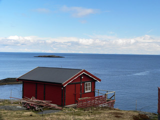 Landscape of single colorful village fishing house on coast of sea in Norway with mountains in...