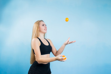 young fun, sweet and joyful girl who plays juggling with mandarins in black tracksuit shorts and a t-shirt on a blue background with a smile on my face copyspase