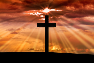 Jesus Christ wooden cross on a scene with dark red orange sunset, twilight light in the background, dramatic sky, clouds, sun rays, sunbeams. Christian Easter, resurrection,Good Friday concept 