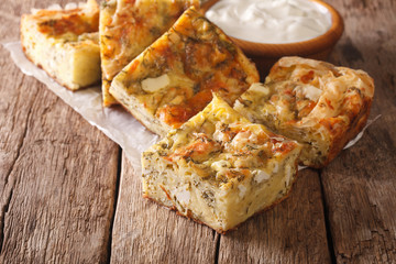 Sliced Serbian Gibanica with cheese, eggs and herbs close-up and yogurt in a bowl. horizontal