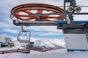 Rote Umlenkscheibe einer Sesselbahn mit Bergstation und verschneiten Berggipfeln vor blauem Himmel