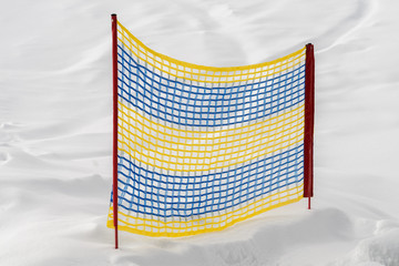Gelb und blauer Fangzaun an einem Berghang mit weißem Schnee