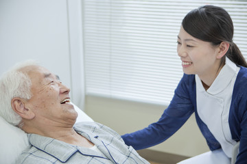 Senior man lying on bed talking to nurse, Kanagawa Prefecture, Honshu, Japan