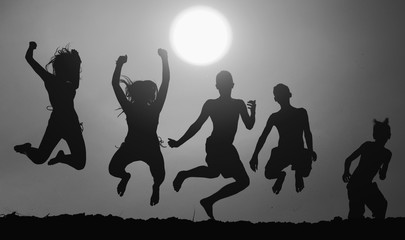 Obraz premium Silhouettes of five teenage boys and girls jumping in the air on the beach against sunset sky on beautiful summer day