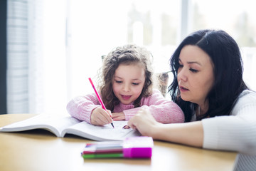 Beautiful school girl doing homework with mother at home