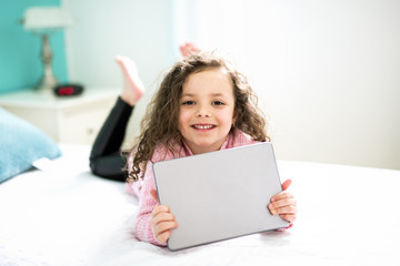 Technologies become easier. Cute little girl holding digital tablet and smiling while lying in bed.