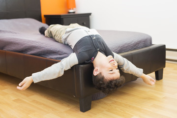 Playful little boy in bed upside down