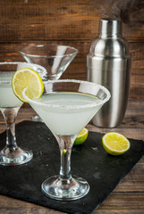 Alcoholic cocktail - gin tonic, martini, margarita. Decorated with slice of lime, with a shaker on a black slate on a wooden table, copy space, vertical