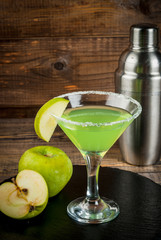 Alcoholic cocktail - Appletini. martini, margarita with apple. Decorated with slice of green apple, with a shaker on a black slate on a wooden table, copy space, vertical
