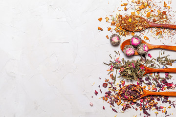 Dry tea in wooden spoons on grey background, top view. Leaves of red, fruit , green and black tea with  fruits and spices