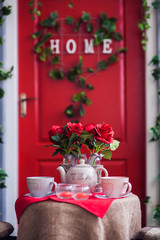 Porch with red door and climbing ivy on the wall. Wicker rocking chair at the spring terrace. Front view
