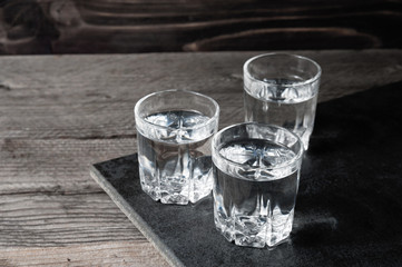 Vodka shots with ice cubes on black stone,