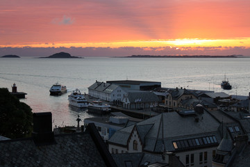 Abendstimmung mit Sonnenuntergang am Hafen von Alesund, Norwegen, mit Leuchtturm, Schiffen und vorgelagerten Inseln im Atlantik