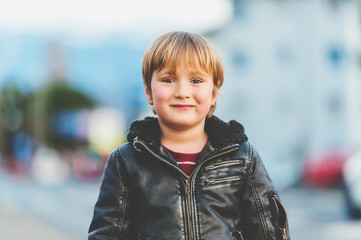 Outdoor portrait of handsome 5-6 year old little boy wearing black leather jacket