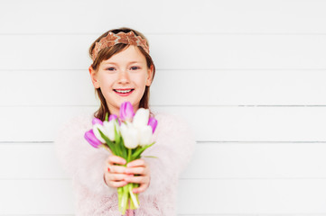 Spring easter portrait of beautiful little girl with tulip flowers, wearing vintage headband and fluffy texture cardigan, standing against white wooden background