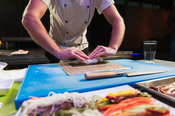 Male hands touch bamboo mat. Small mat on cooking board. Japanese chef at work. Man prepares sushi rolls.