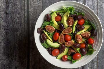 Large fresh salad in white bowl on wood surface
