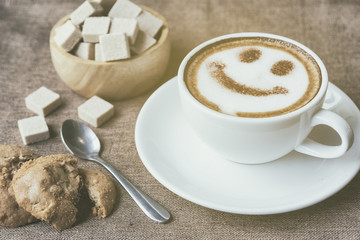 A cup of cafe latte with coffee beans and cookies