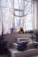 White wooden board stairs below spring windows with lightning bulbs garland. Lavender flowers and Teddy bear