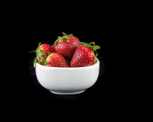 White bowl of whole red Strawberries on a black background