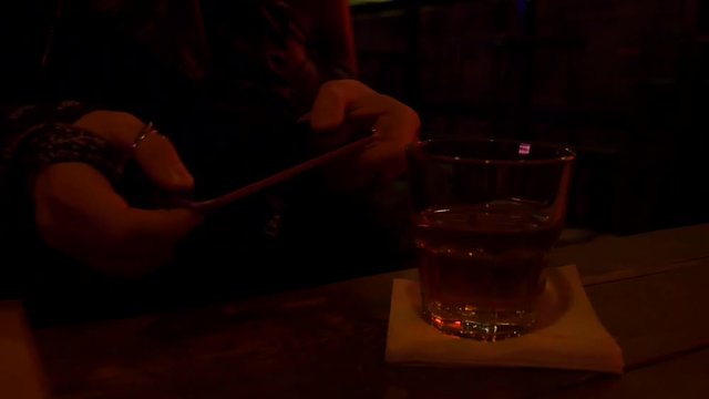 Nice female hands are holding a mobile phone in restaurant. Bar stand with drinks, menu, sign, glass. Red light and glow. Slow motion