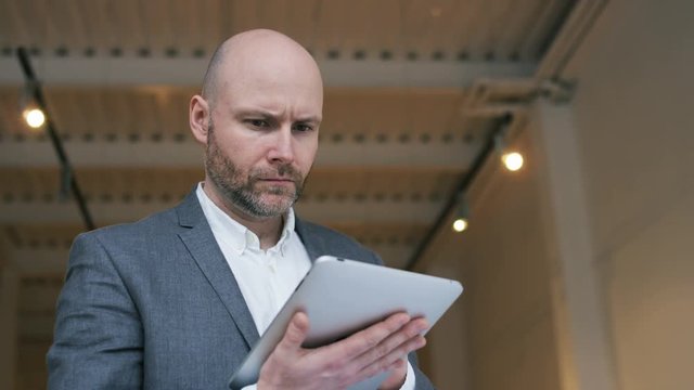 Middle-Aged Bald Businessman Using a Tablet Computer