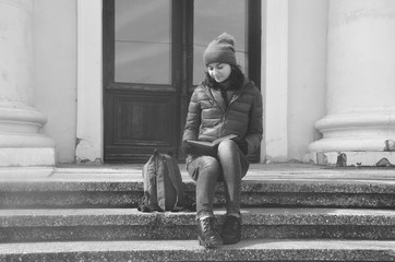 A beautiful young woman sitting on stairs and reading a book