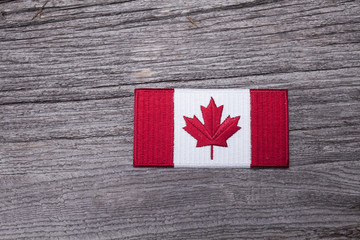An embroidered Canadian flag patch sits on a rustic wooden background.