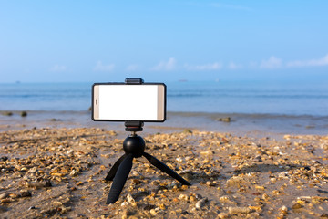 mobile smartphone on tripod put on sand beach have sea and sky background