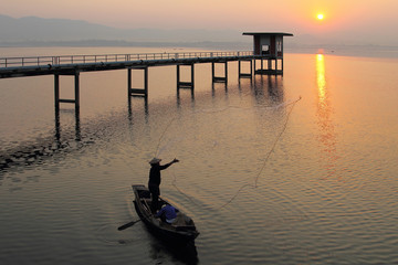 Silhouette of fishermen using nets to catch fish at the Bangpra lake with beautiful scenery of nature during sunrise time. Bang Pra Reservoir at Chonburi province in Thailand