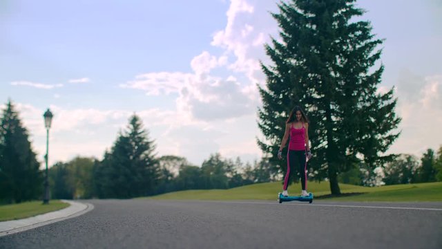 Happy girl ride gyro scooter on asphalt road at park. Girl on two wheel electric scooter. Fitness woman ride on mini segway in city park. Smiling woman riding on self balancing hover board