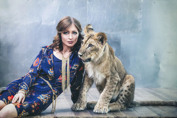 Beautiful fashionable young woman with a little alive lion cub