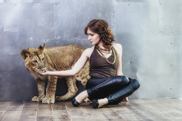 Obraz premium Beautiful fashionable young woman with a little alive lion cub
