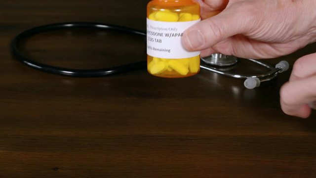 Oxycodone opiate tablets being spilled onto a doctor's table with a stethoscope in the background to illustrate the problems of opioid addiction